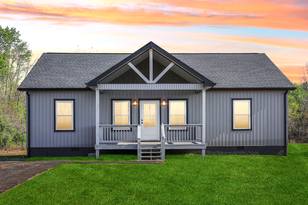 Small gray house with white trim, front porch, and lit windows at sunset