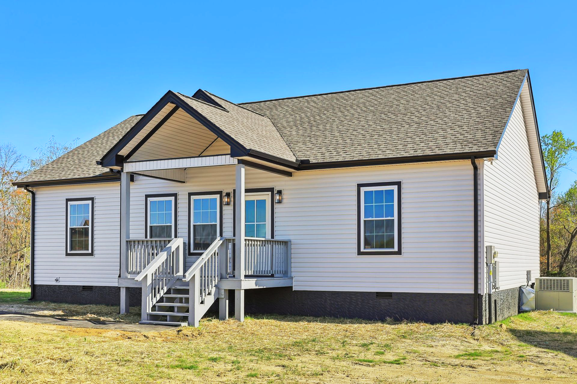 Single-story white house with gray roof and front porch steps under a clear blue sky