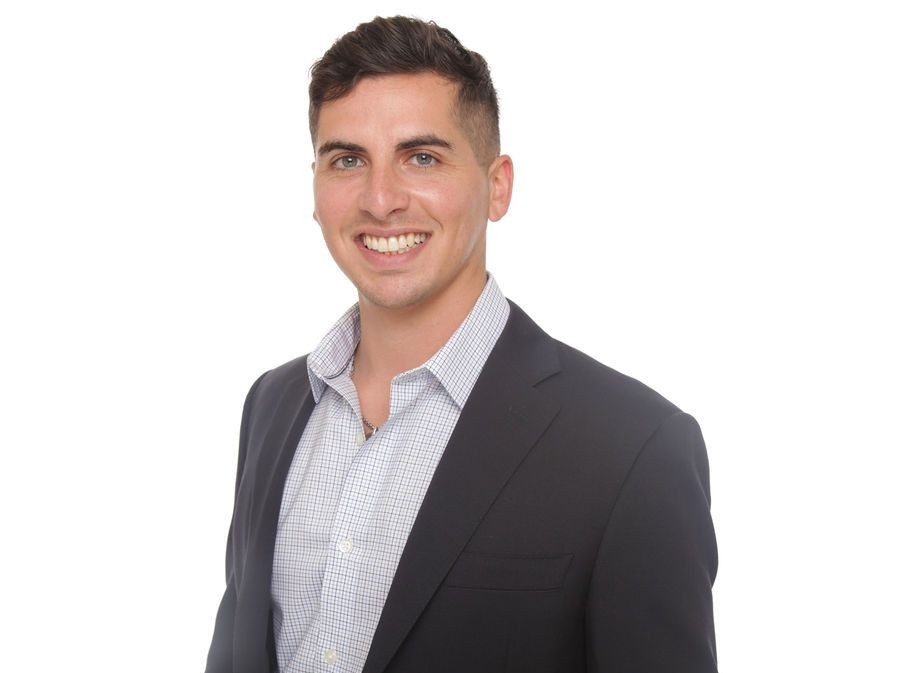 Smiling person in a dark blazer and light patterned shirt against a white background
