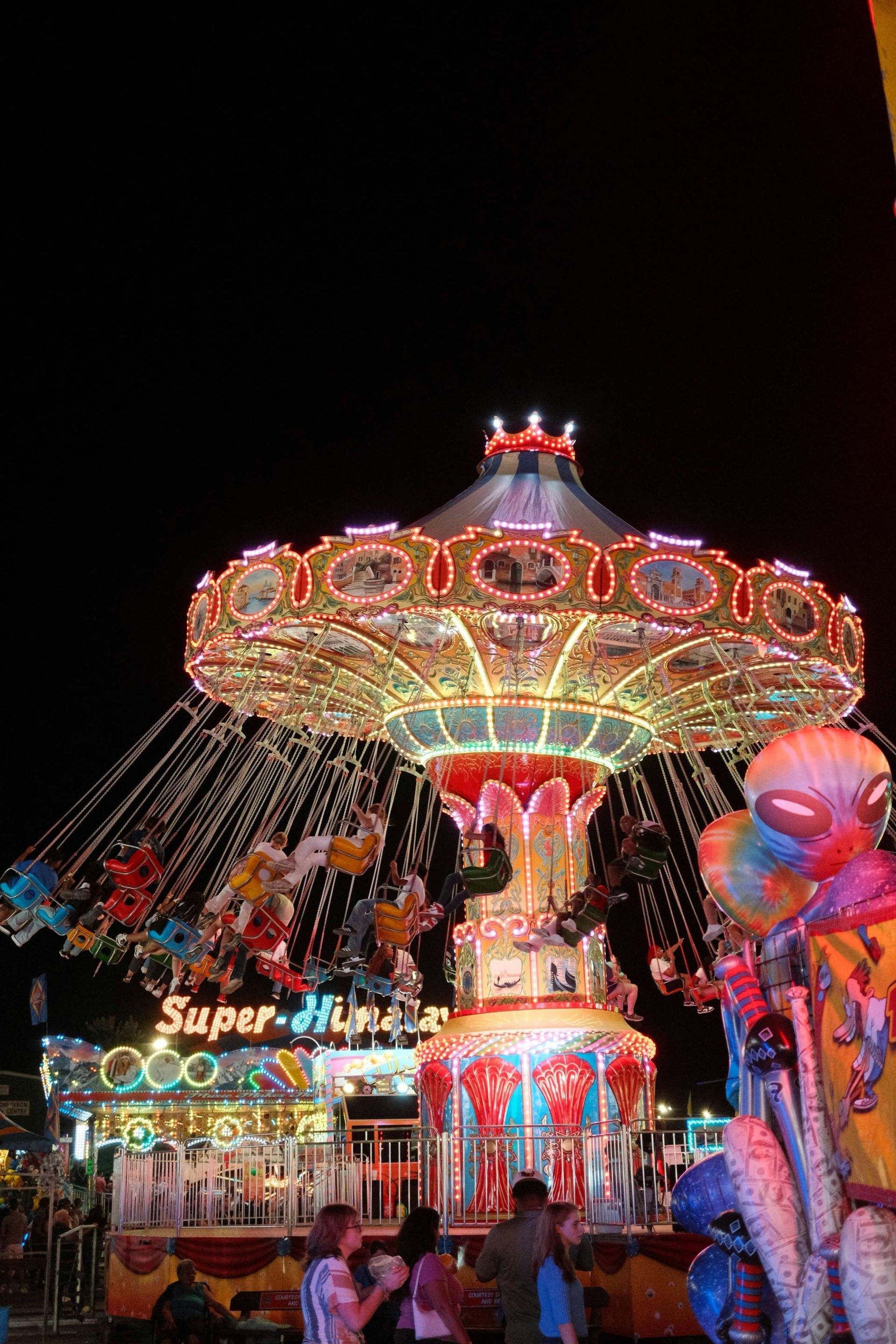 Illuminated carnival swing ride at night with colorful lights against a dark sky