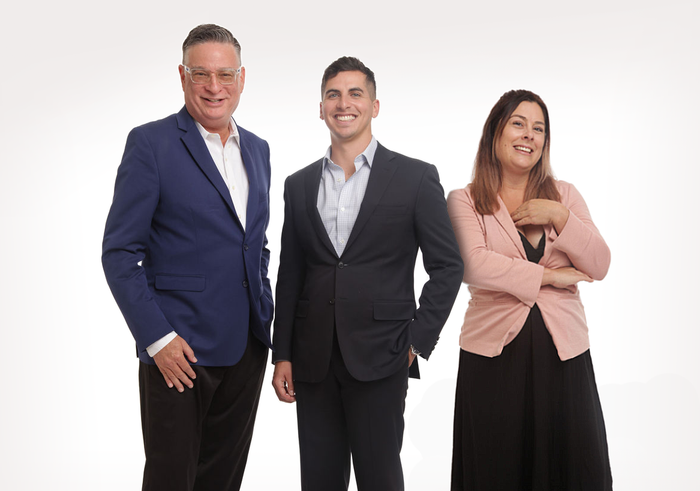 Three business professionals posing against a white background, smiling and standing together.