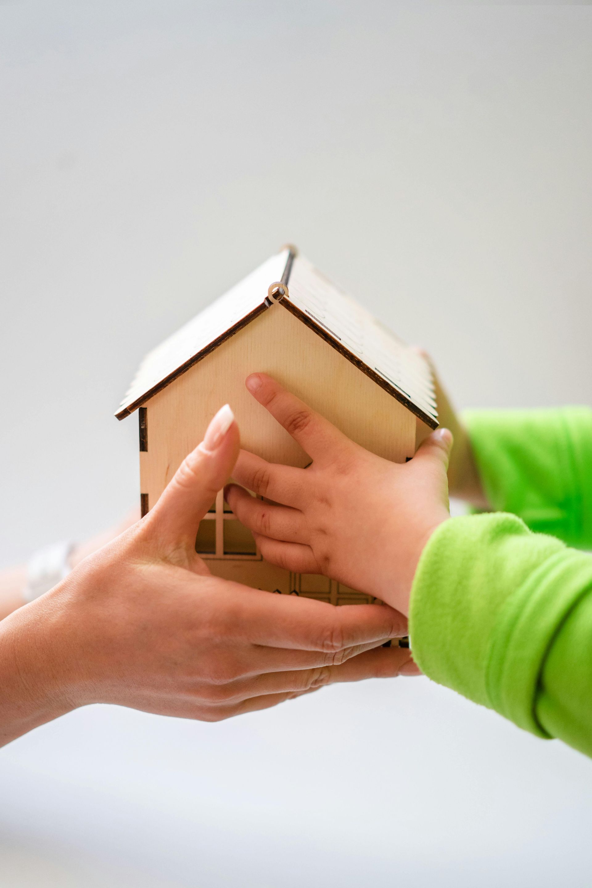 Adult and child hands holding a small cardboard house model
