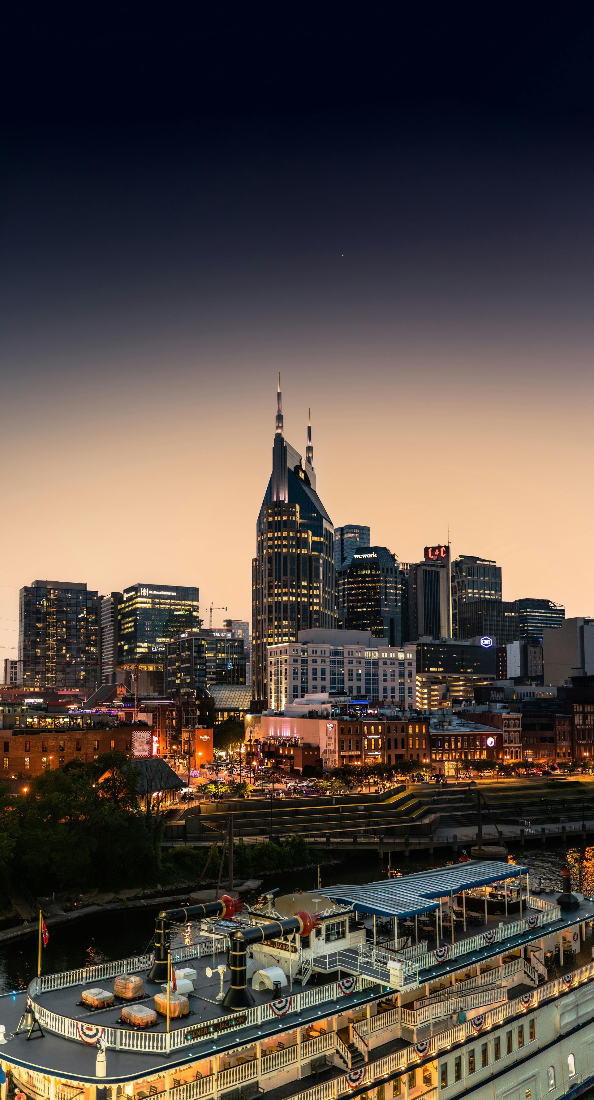 City skyline at dusk with a lit high-rise and bridge over a river in the foreground