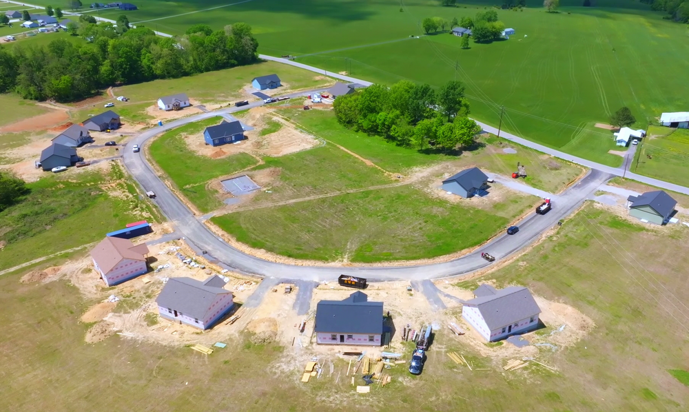 Aerial view of a curved rural housing development with several houses, roads, and green fields.