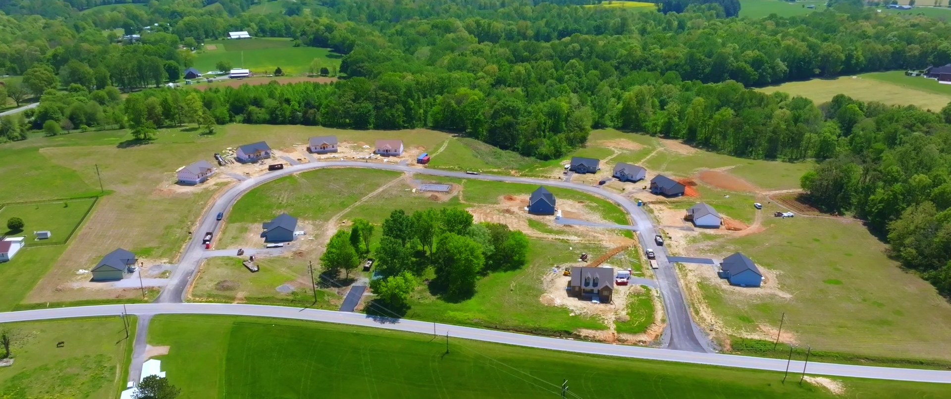 Aerial view of a suburban construction site with multiple houses under construction amid green fields.