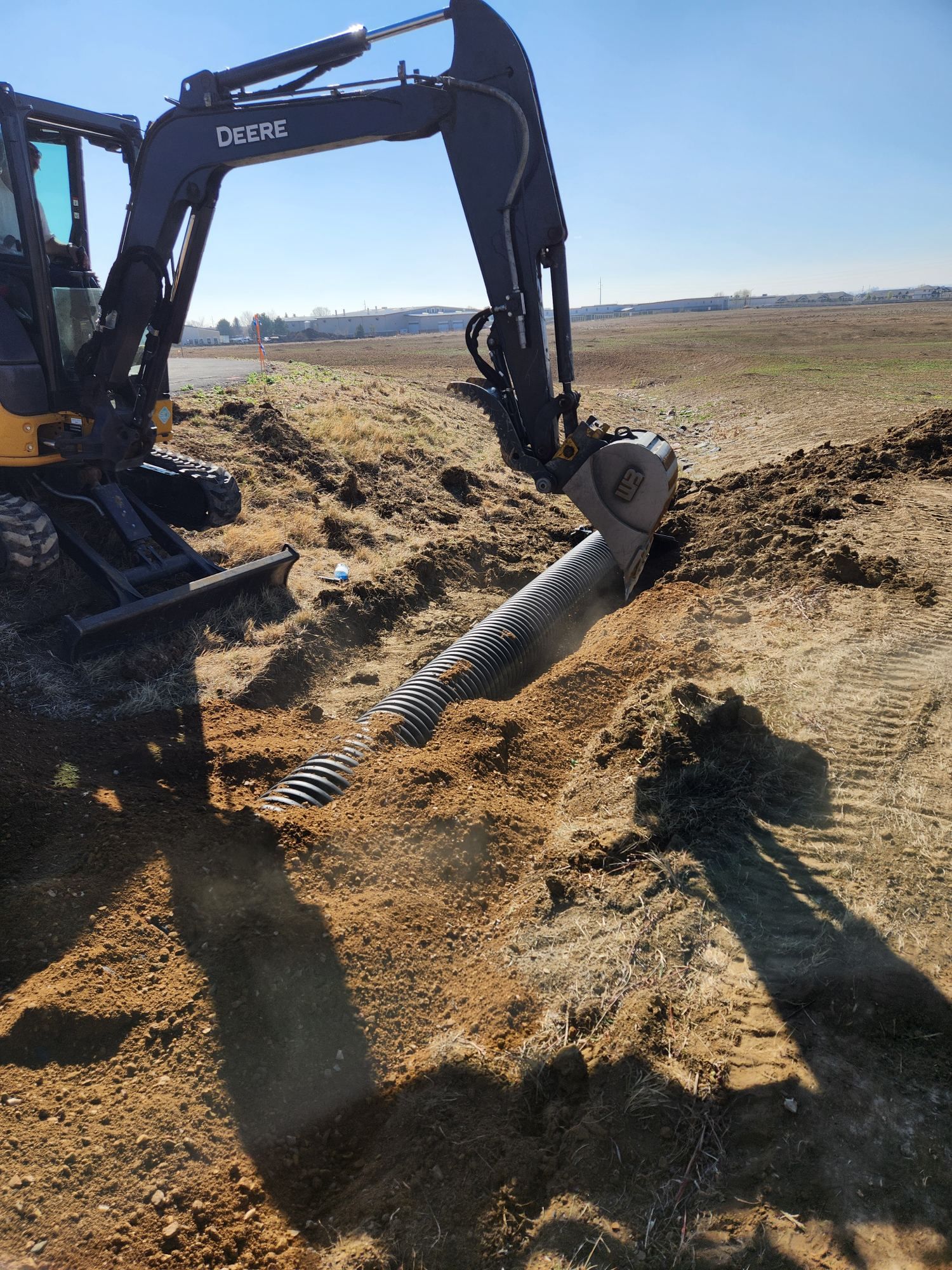Excavator digging soil in a muddy field under a clear sky