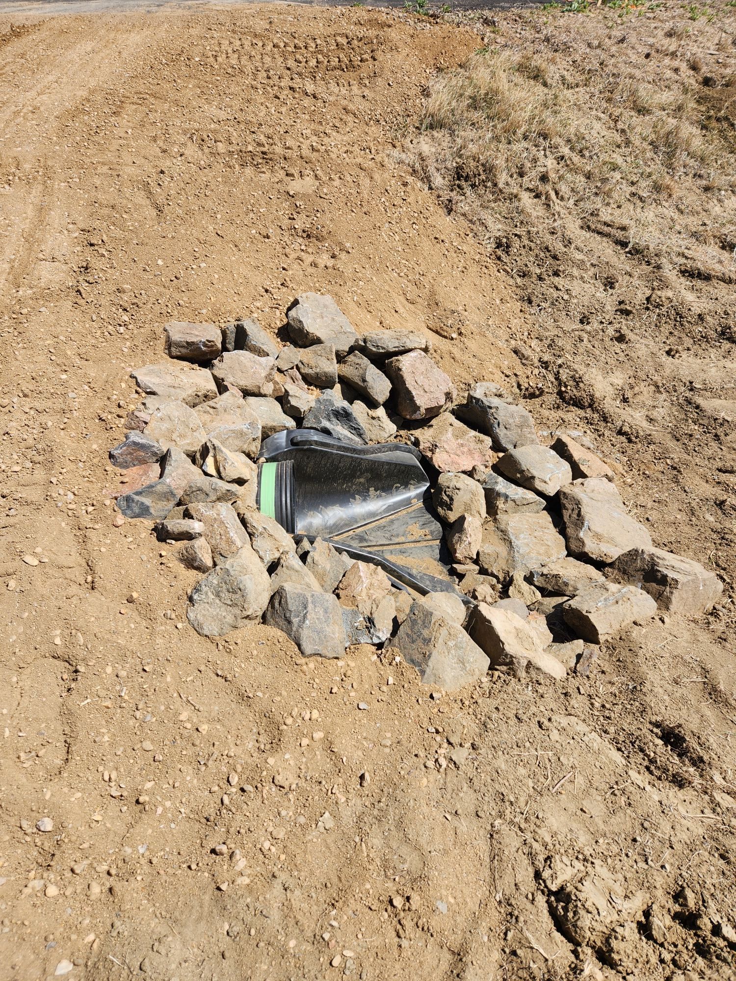 Small rocky fire pit with a shiny metal can in a dry sandy field