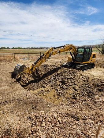 Workers dig a trench in a backyard. A small excavator is in the foreground. A house, shed, and grill are in the background.