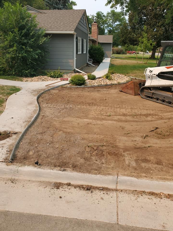 A construction site. A house with a concrete sidewalk and a small bobcat on dirt.