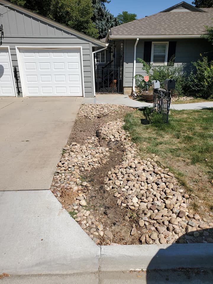 Driveway with rock-filled drainage channel between garage and lawn.