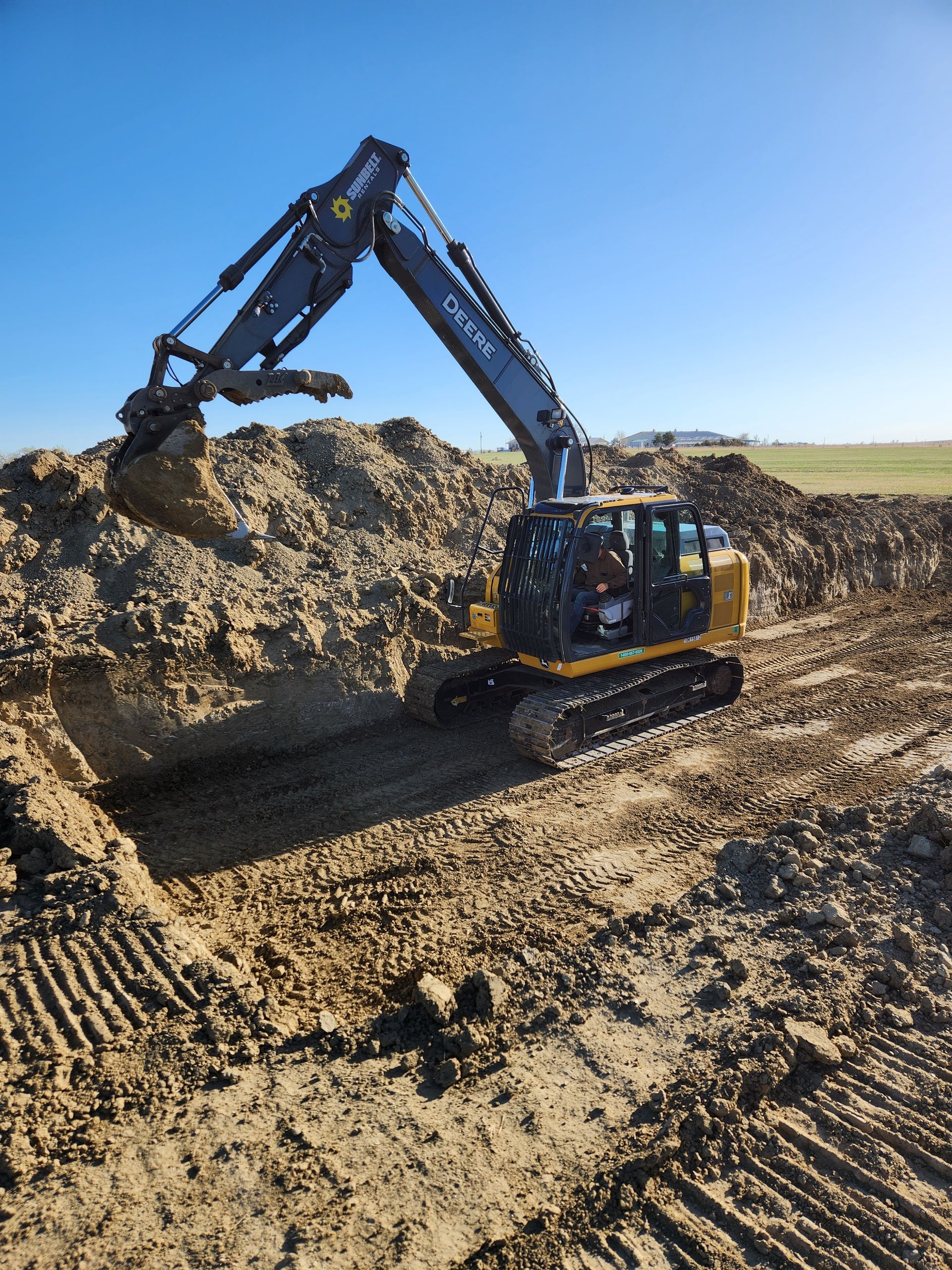 Yellow excavator digging in a dirt pit under a blue sky.