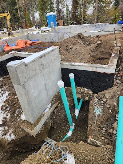 Construction site: foundation with plumbing, dirt, snow, concrete walls, and a portable toilet.