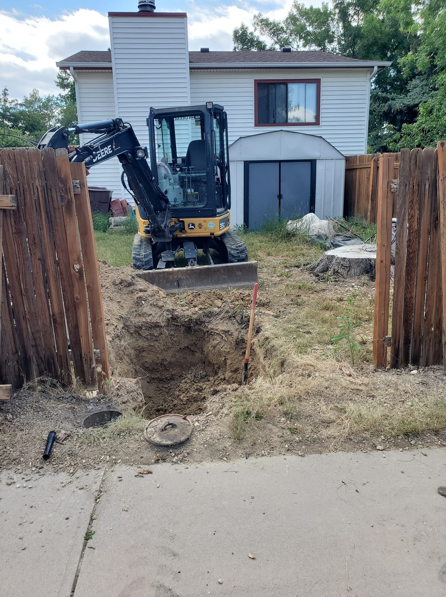 Mini excavator digging in a backyard, fence on either side.