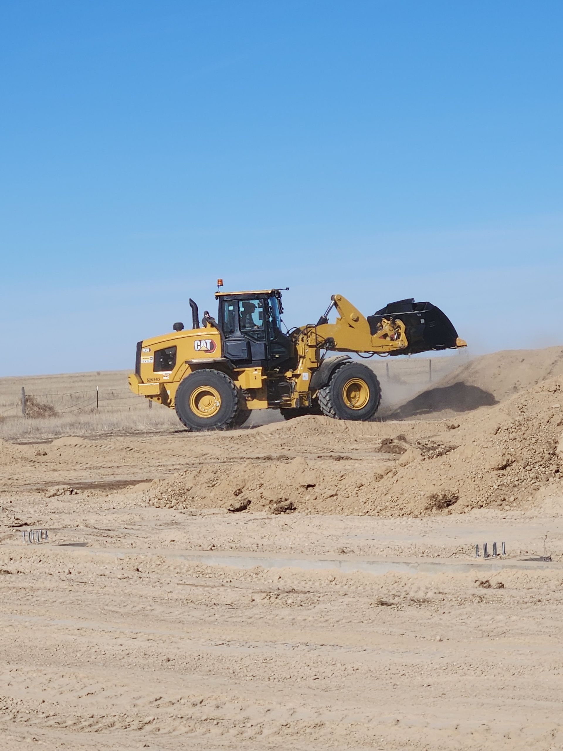 Yellow front loader driving through sandy desert under a clear blue sky