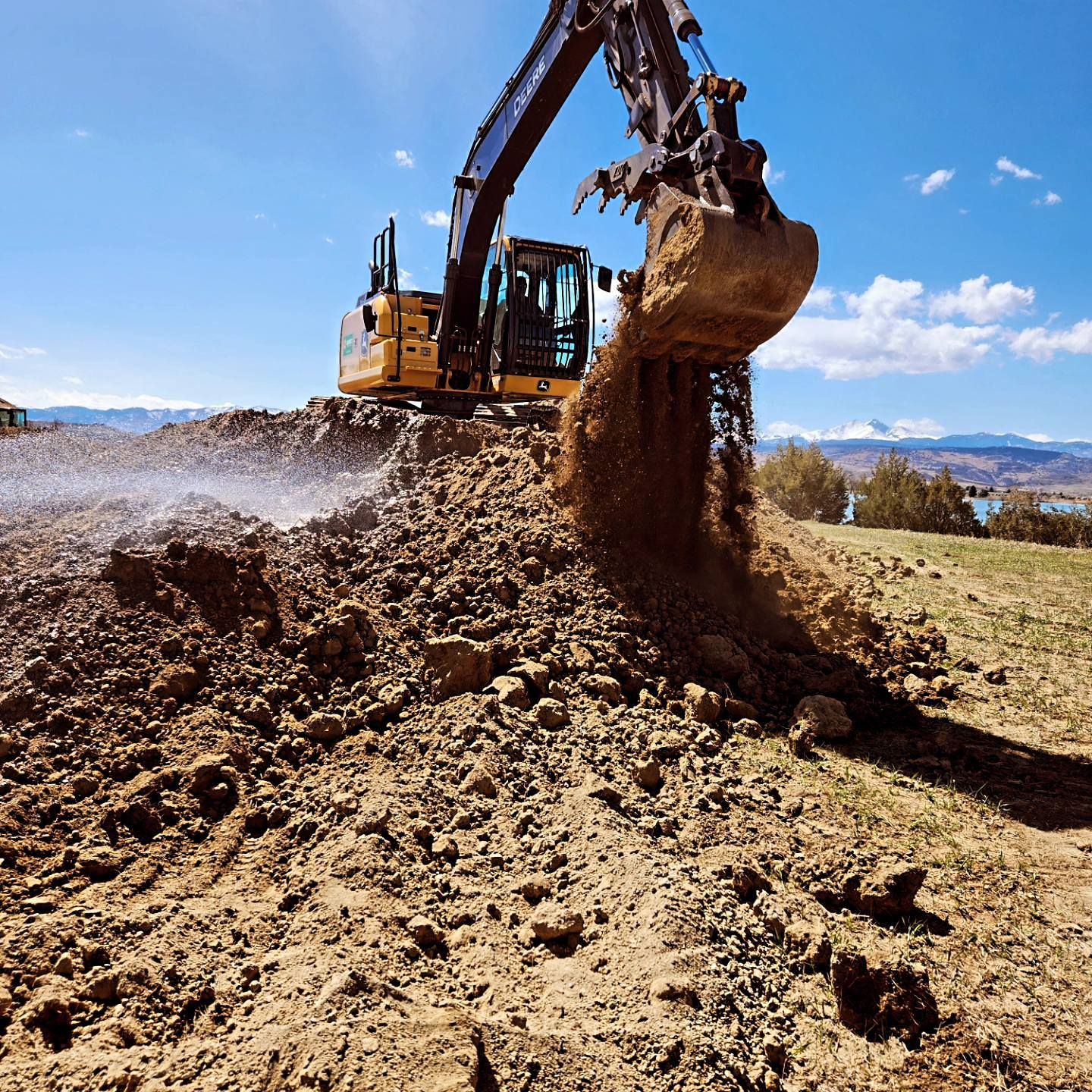 Yellow excavator digging dirt on a sunny day. Brown earth piles in front of the machine.