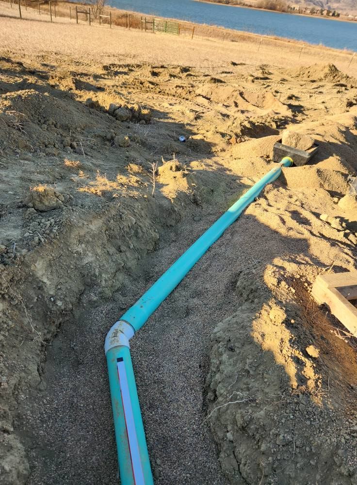 A turquoise pipe runs through a gravel-lined trench in a dirt landscape, likely for underground utilities.