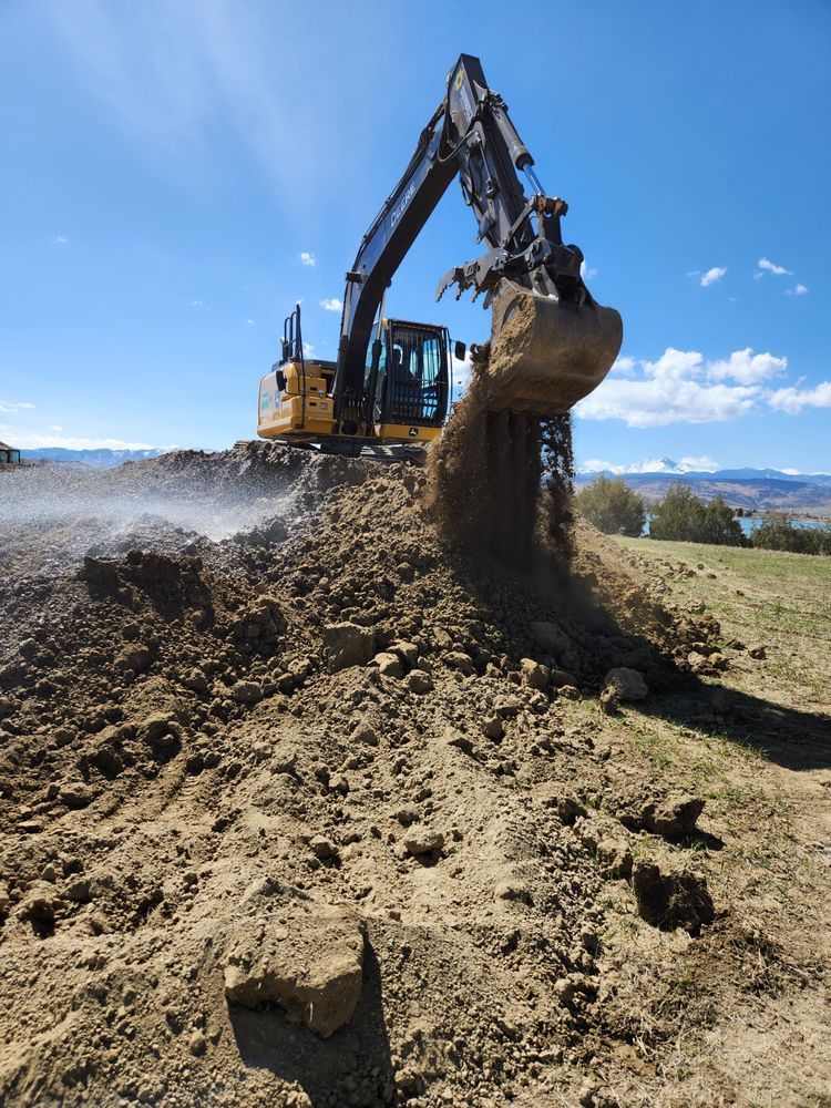 Excavator digging into a mound of earth under a blue sky, dirt falling from the bucket.