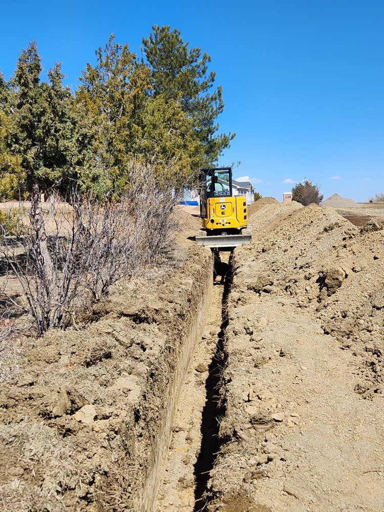 Yellow excavator digging a trench in dirt, sunny day.