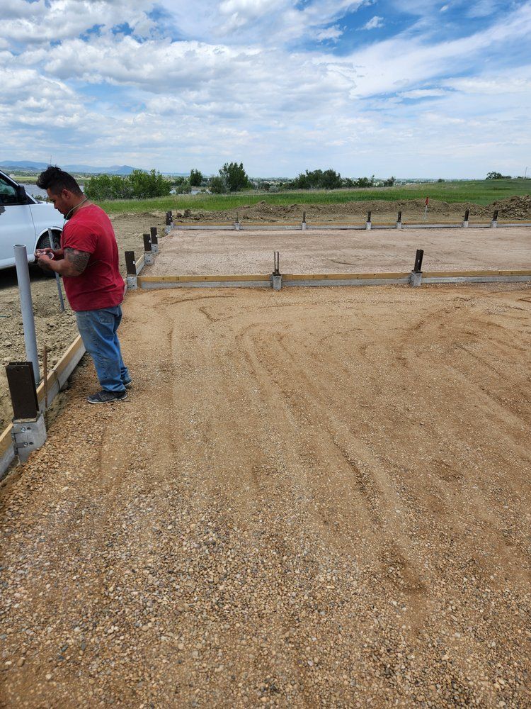 Man in red shirt working on a gravel lot with concrete edges; blue sky with clouds in background.