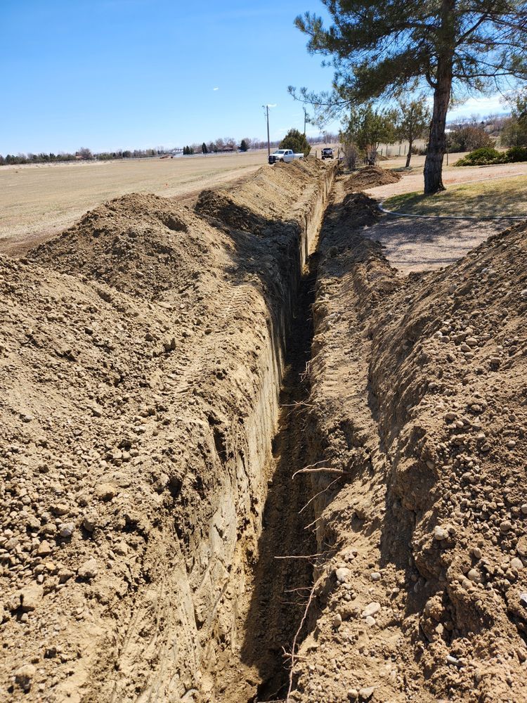 Narrow trench dug in brown soil, stretching into the distance under a blue sky, near a road.