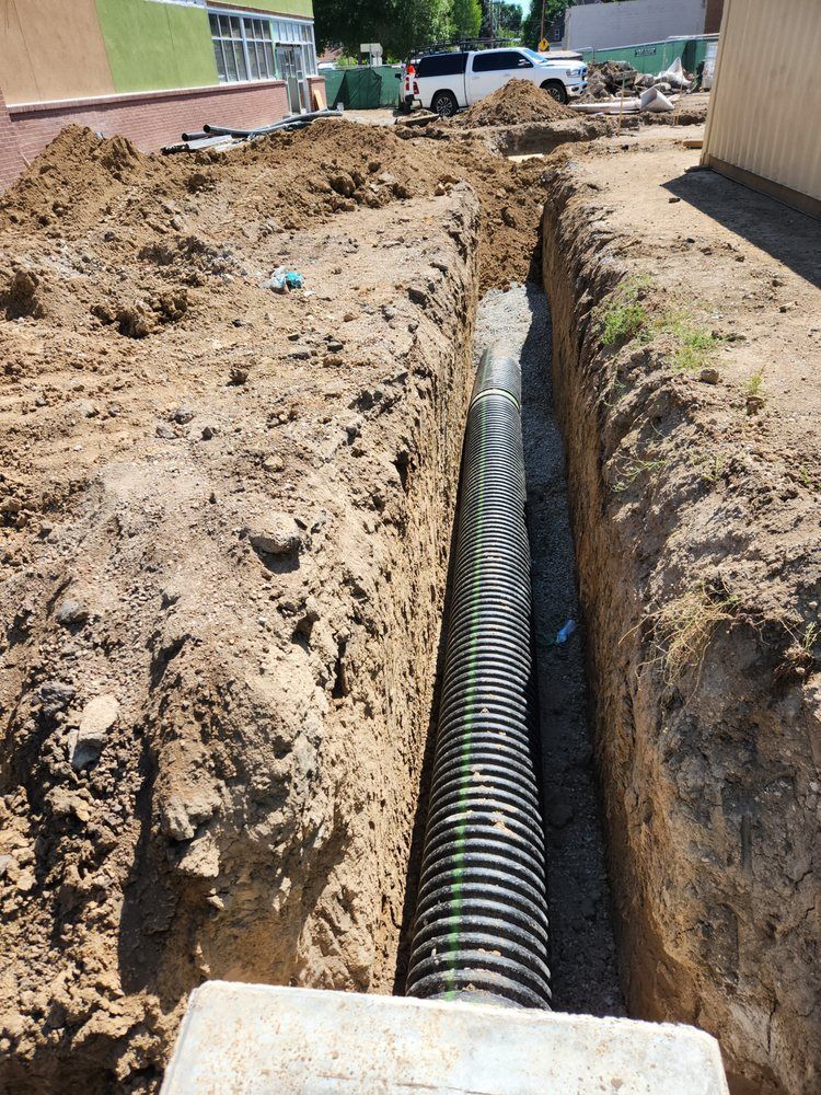 A corrugated drainage pipe installed in a trench. Construction site, dirt, and a vehicle are in the background.