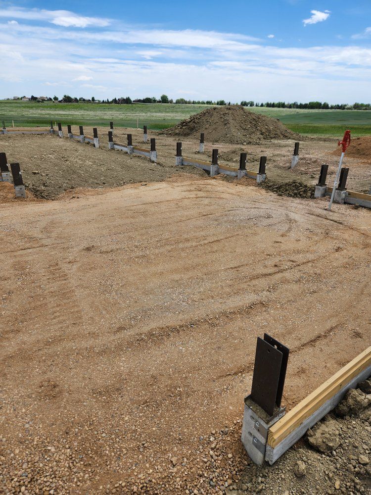 Construction site with concrete piers, dirt, and a pile of earth under a blue sky.