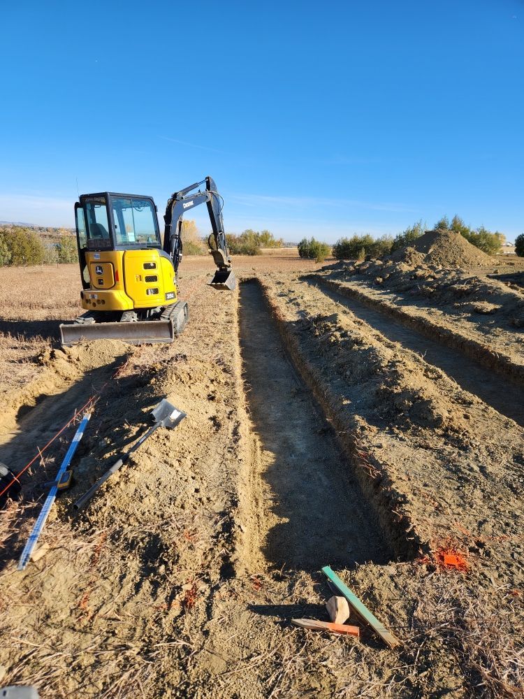 Yellow excavator digging trenches in a field under a clear blue sky.