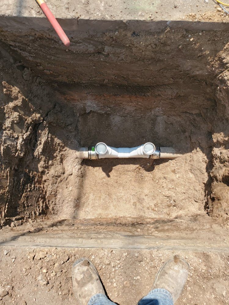 A trench in dirt with exposed white plumbing pipes, viewed from above.