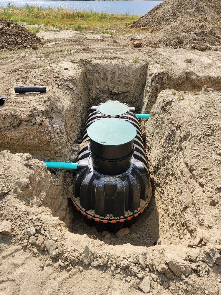 Septic tank installed in a dirt trench, surrounded by soil.  Green lids, blue and black pipes visible.