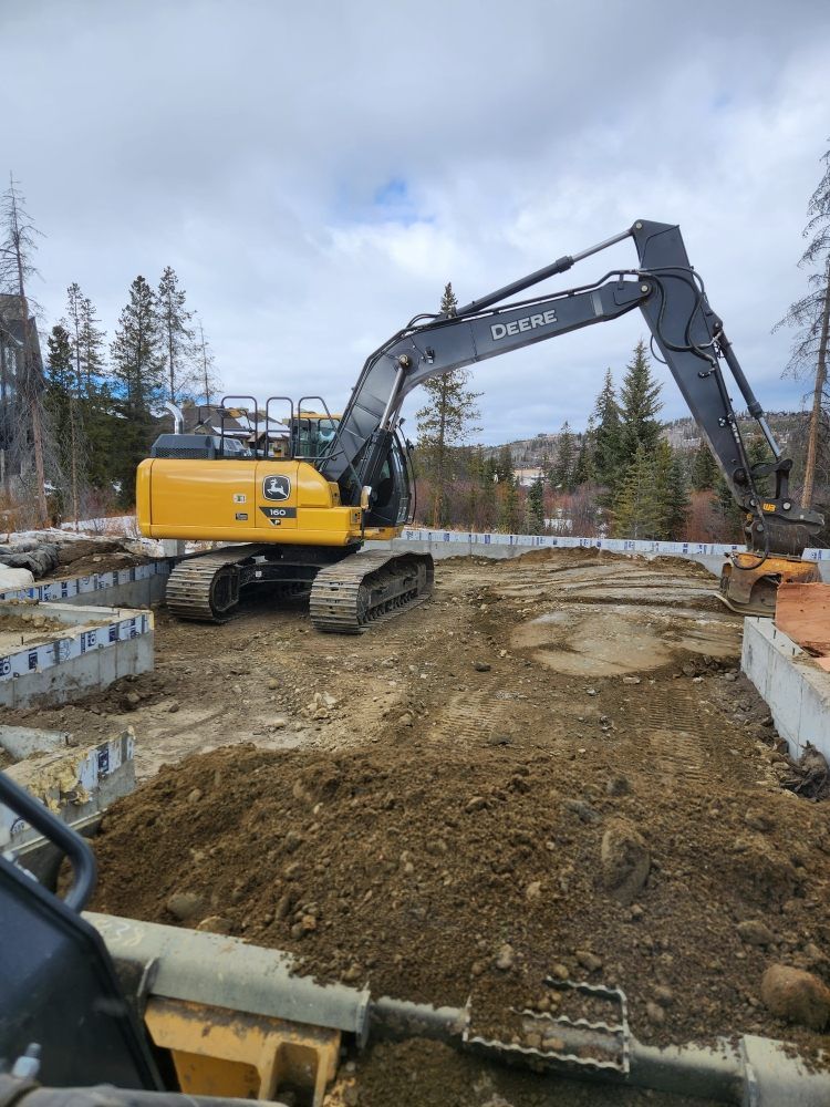 Yellow excavator on a construction site, scooping dirt. Gray cloudy sky in the background.