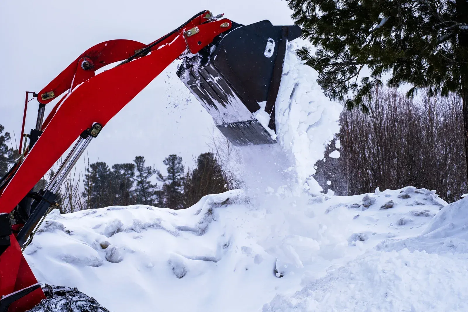 Red excavator dumping snow.