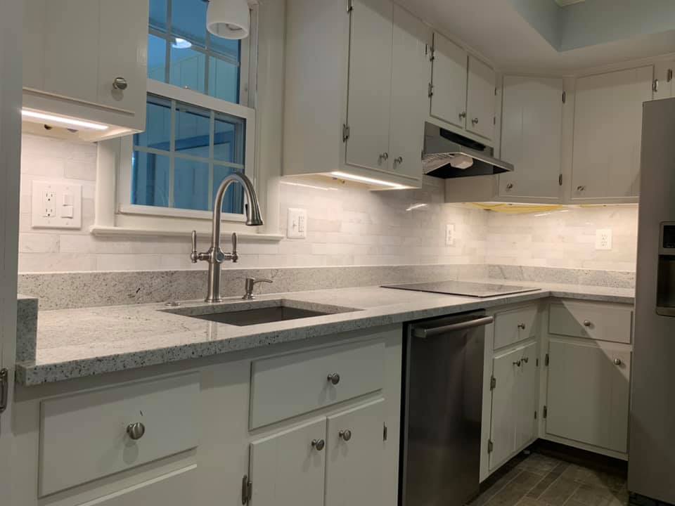White kitchen with granite countertops, stainless steel appliances, and under-cabinet lighting.