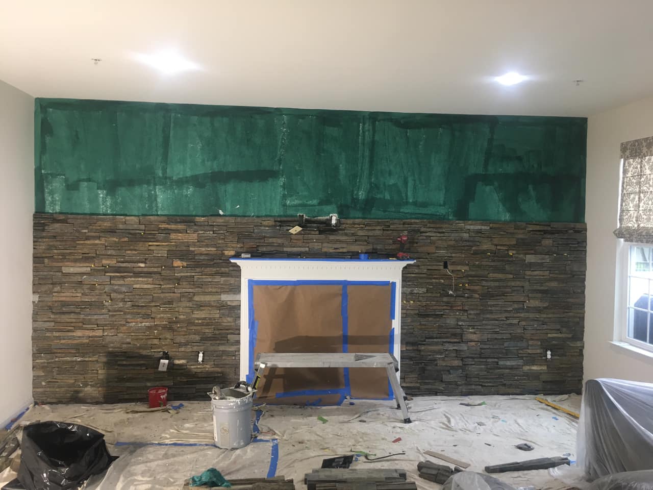 Fireplace being renovated with stone and protective covering. Construction tools and debris visible.
