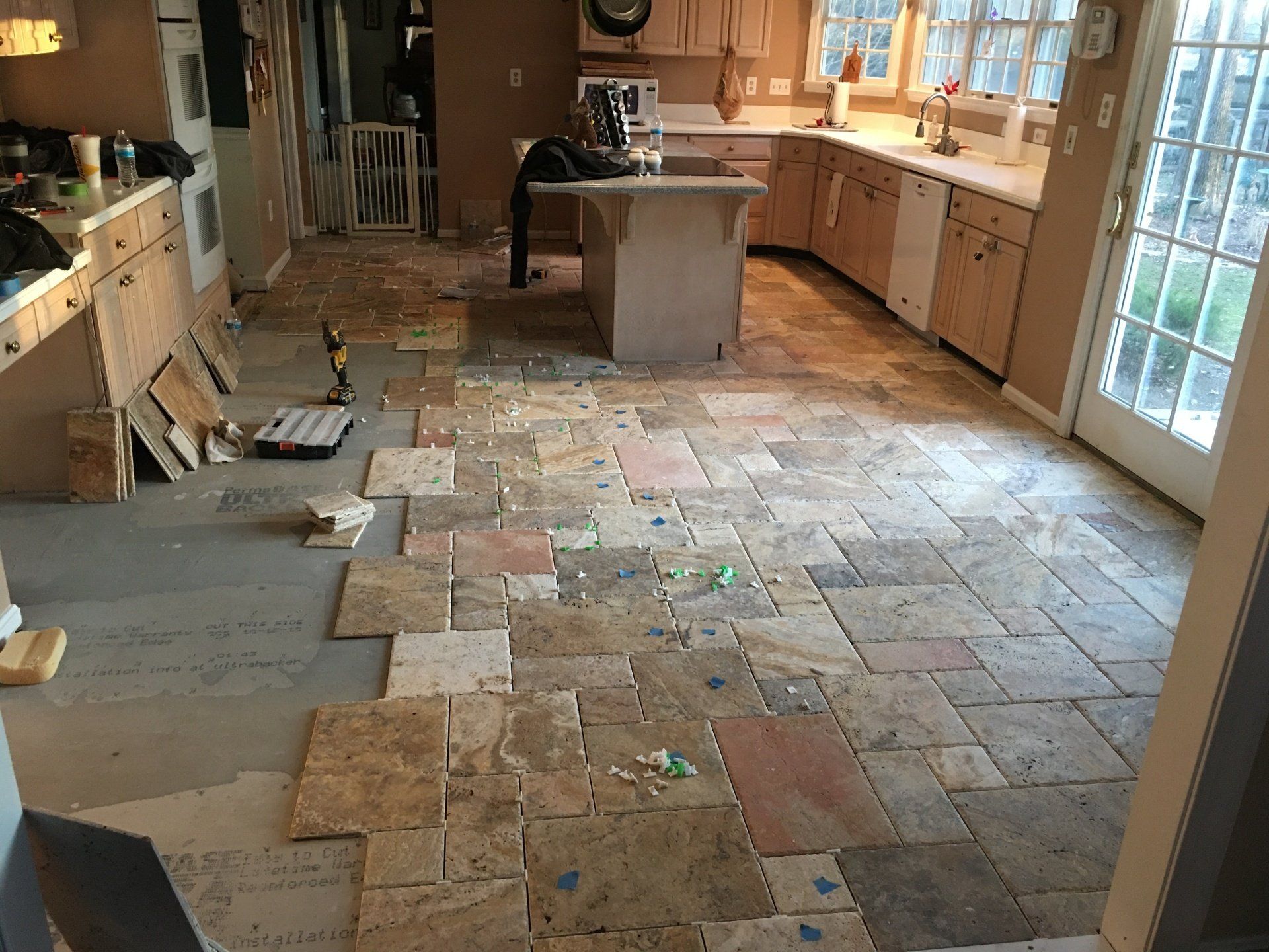 Kitchen with stone tile flooring partially installed; cabinets and island visible.