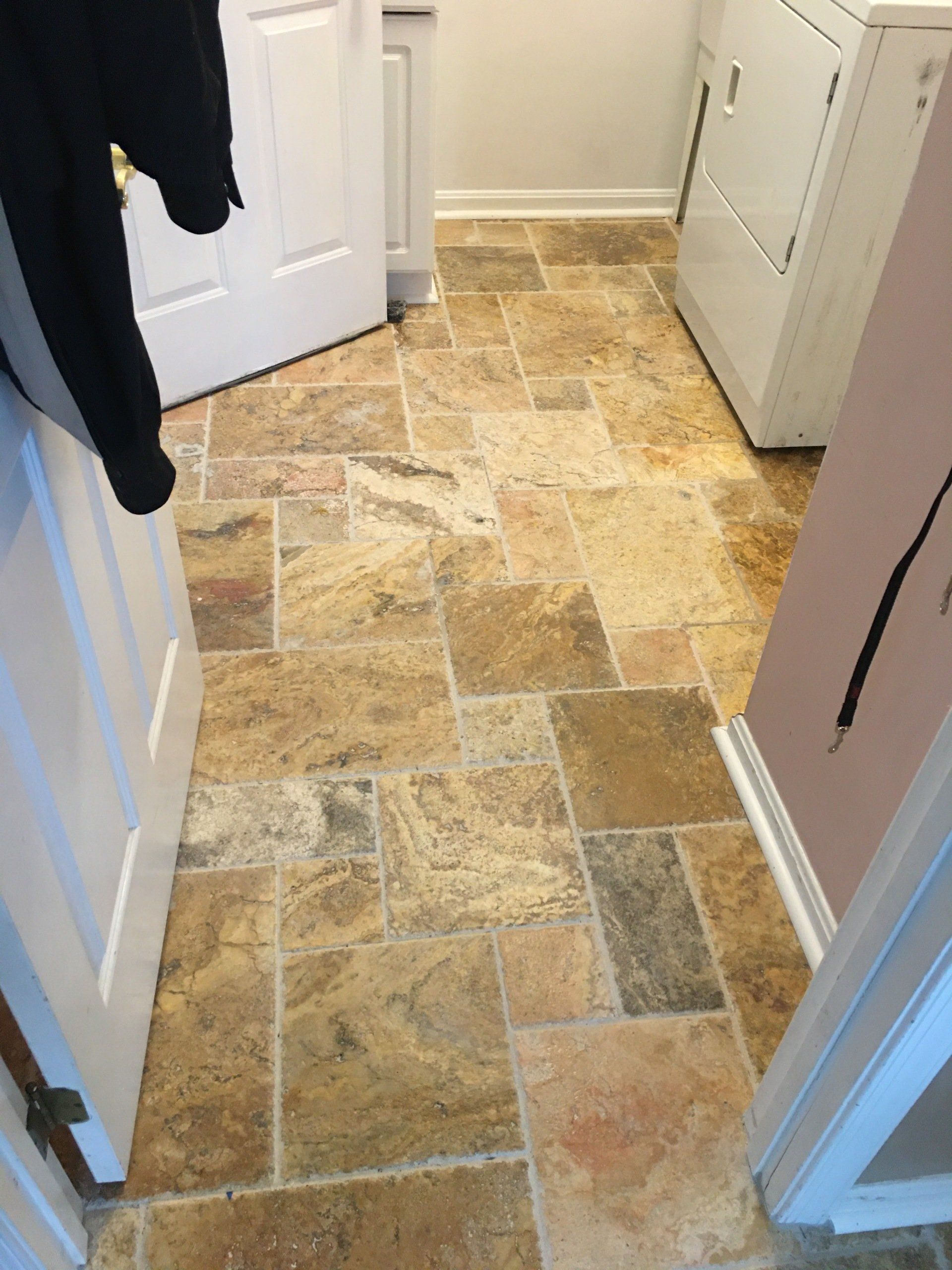 Tiled floor in a laundry room, with a washing machine and door visible. Brown, tan, and gray tiles.
