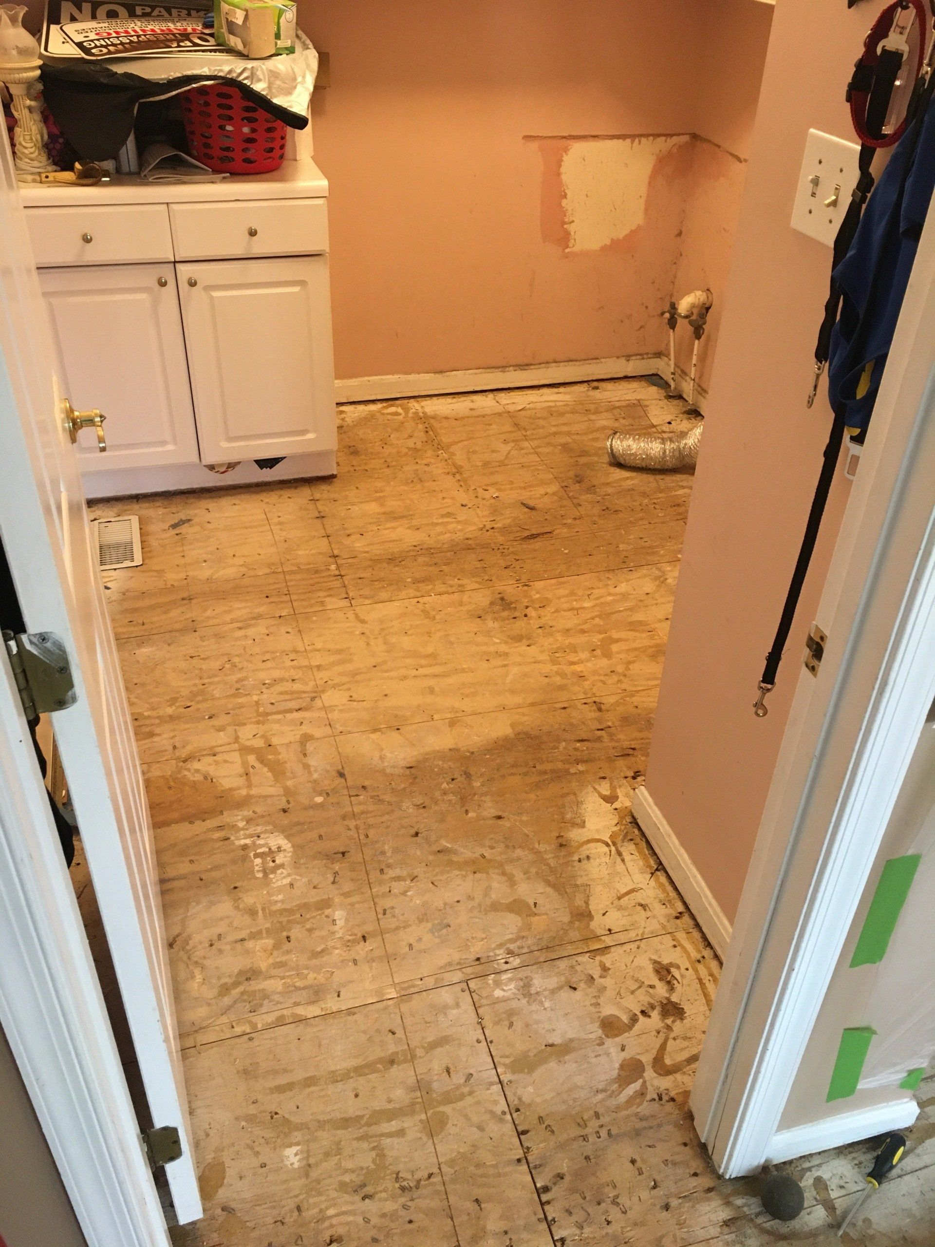 View of a room with floor damage, light pink walls, white cabinets, and an open doorway.