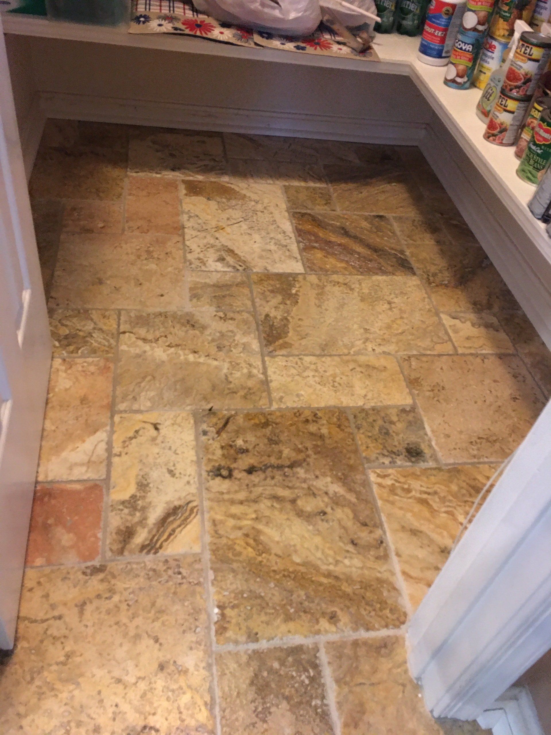 Pantry with beige and brown tile floor. Shelves on right hold canned goods. White door frame on left, pantry entrance.