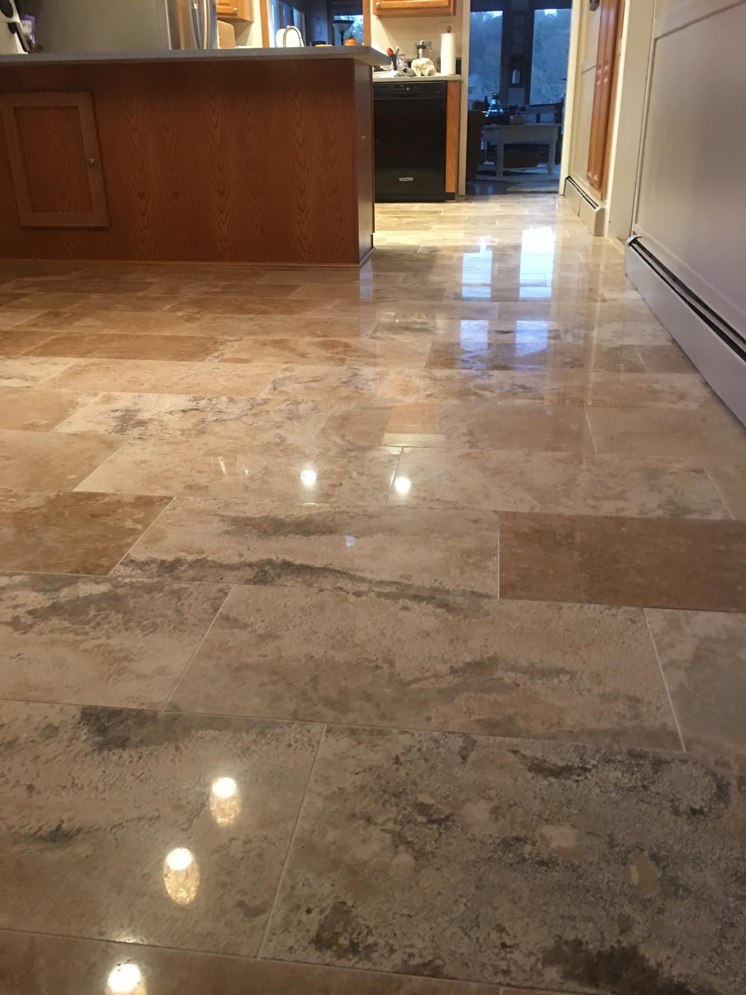 Polished travertine tile floor in a kitchen, with a wooden island and doorway to another room.