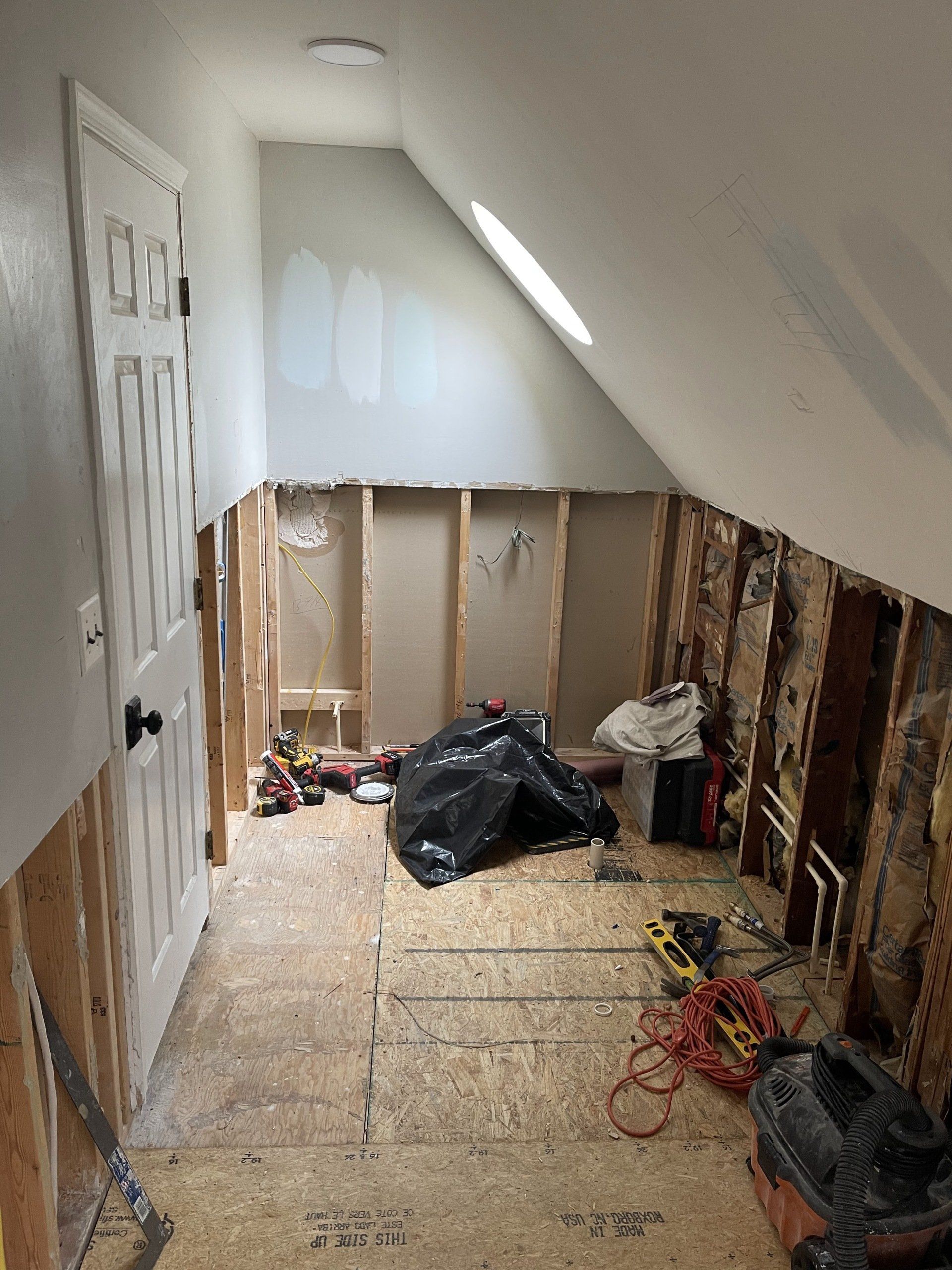 Construction in an attic space. Partially framed walls, door, and tools scattered on the floor.