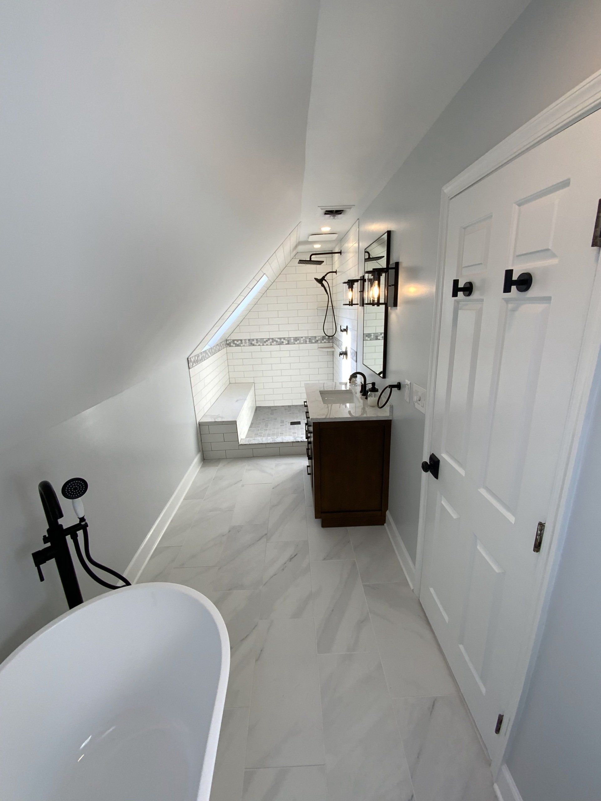 Bathroom with white bathtub, gray tile floor, vanity, and a shower under a sloped ceiling.
