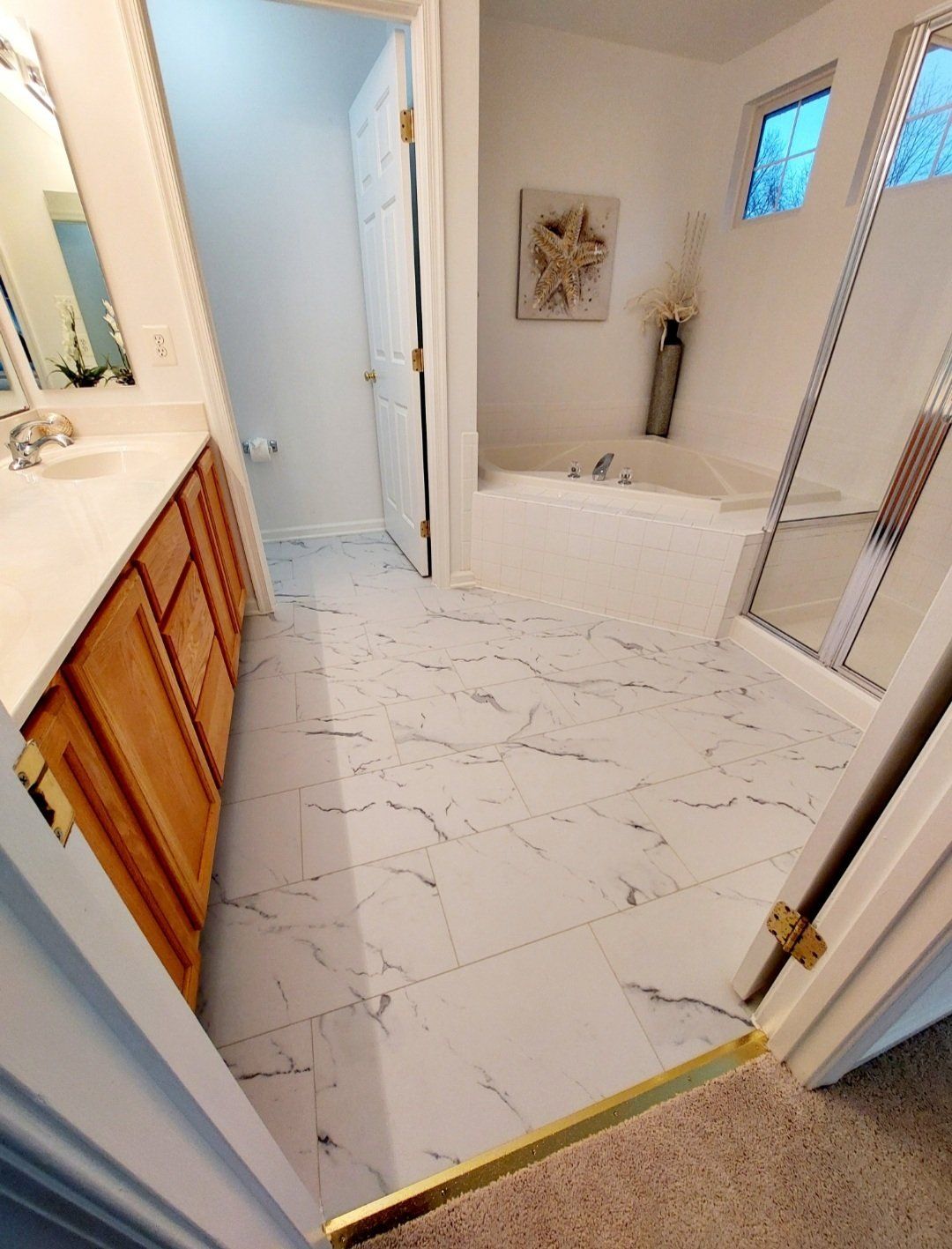 Bathroom with marble tile floors, wooden vanity, and white walls. A large mirror and a doorway are visible.