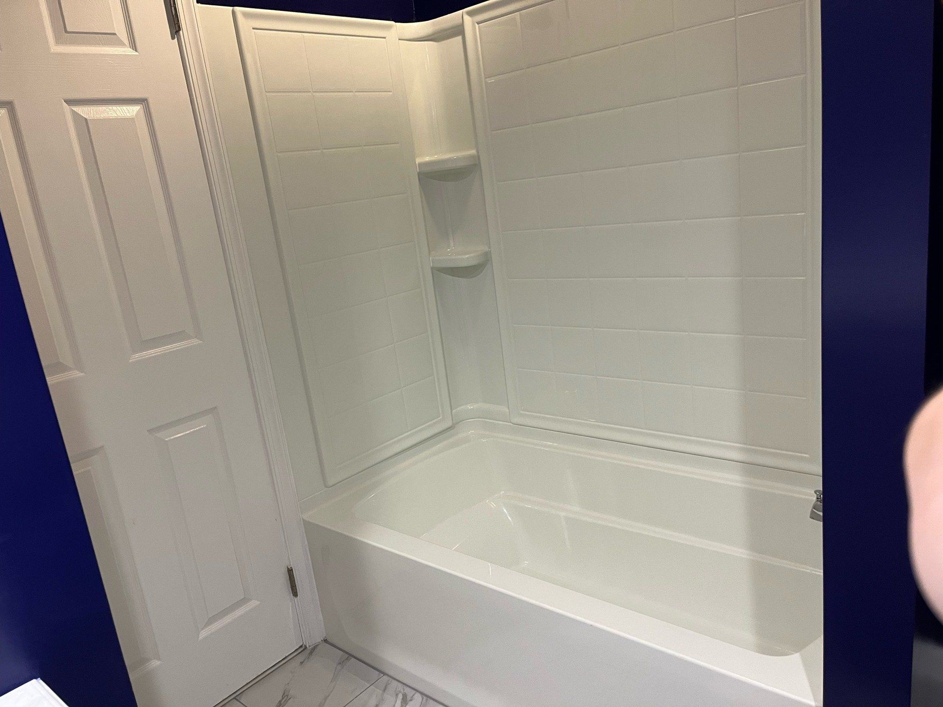 White bathtub and shower surround in a bathroom with a white door and blue walls.
