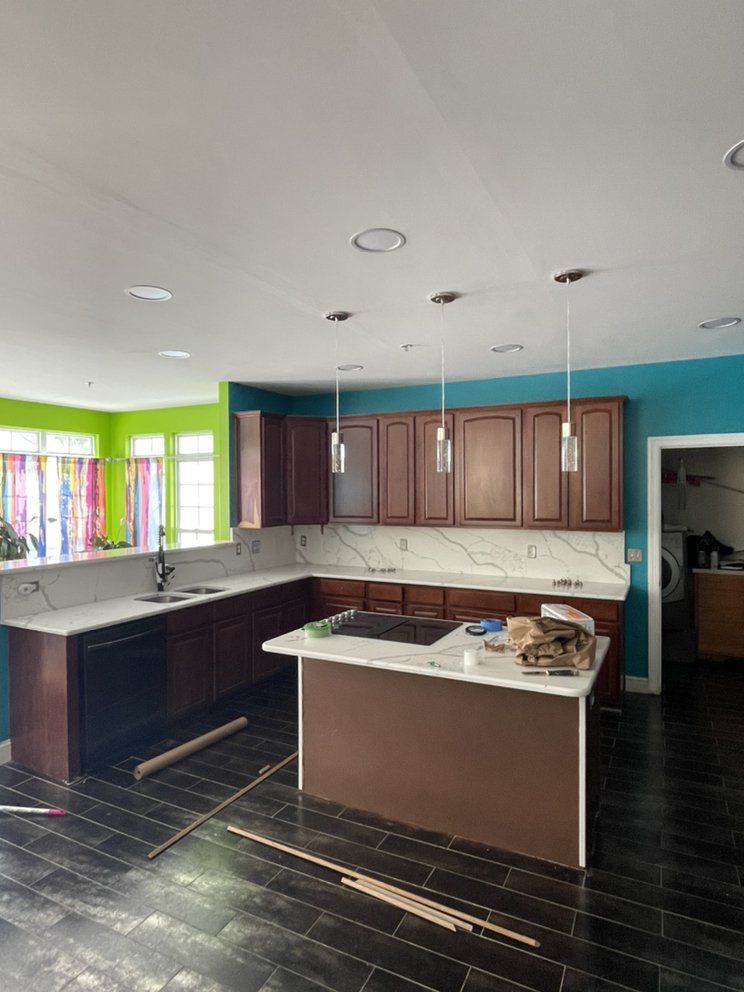Kitchen with brown cabinets, white countertops, and teal and green walls, with dark flooring.