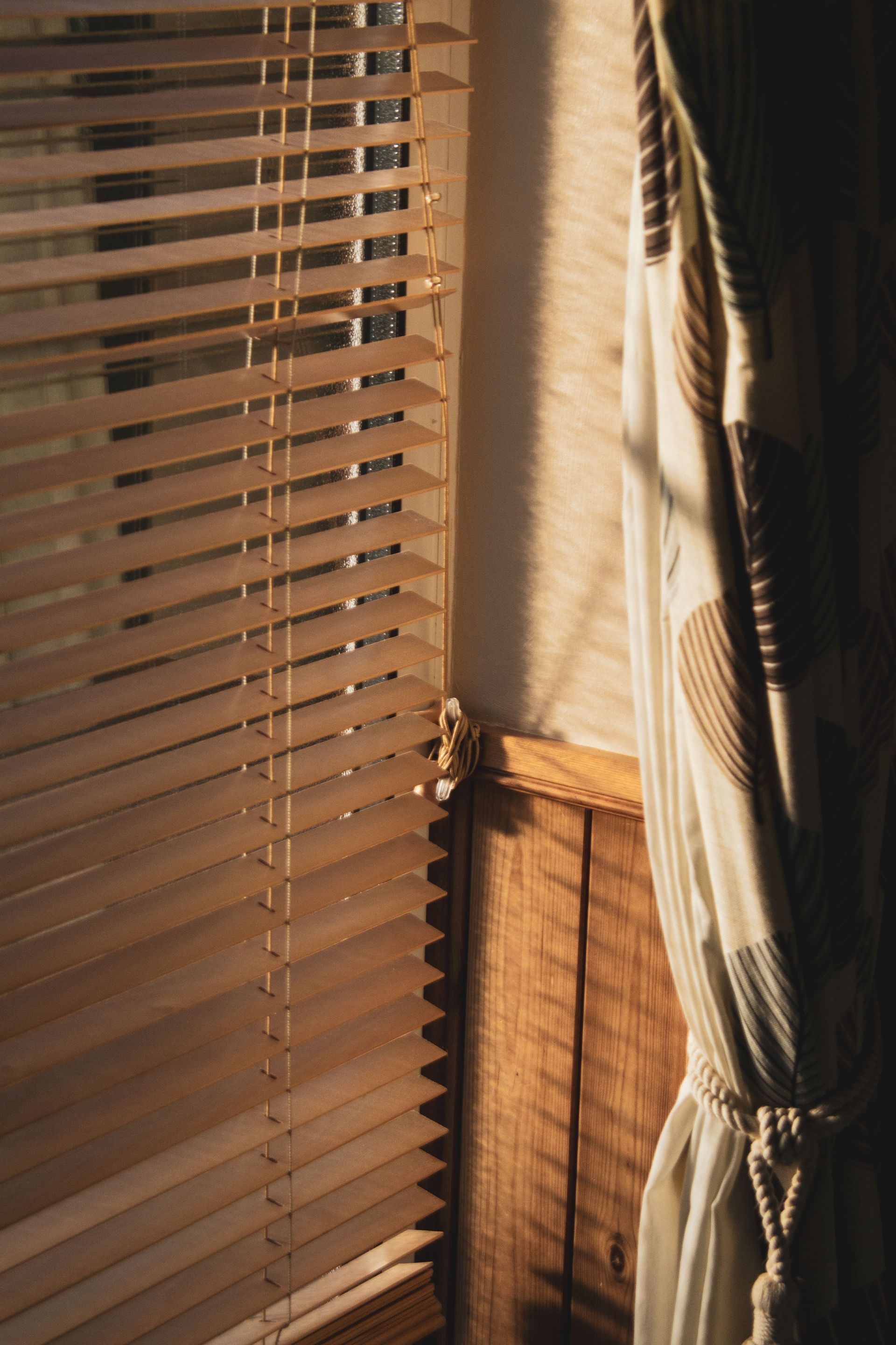 Ventana soleada con persianas de madera y una cortina transparente atada en un interior acogedor.