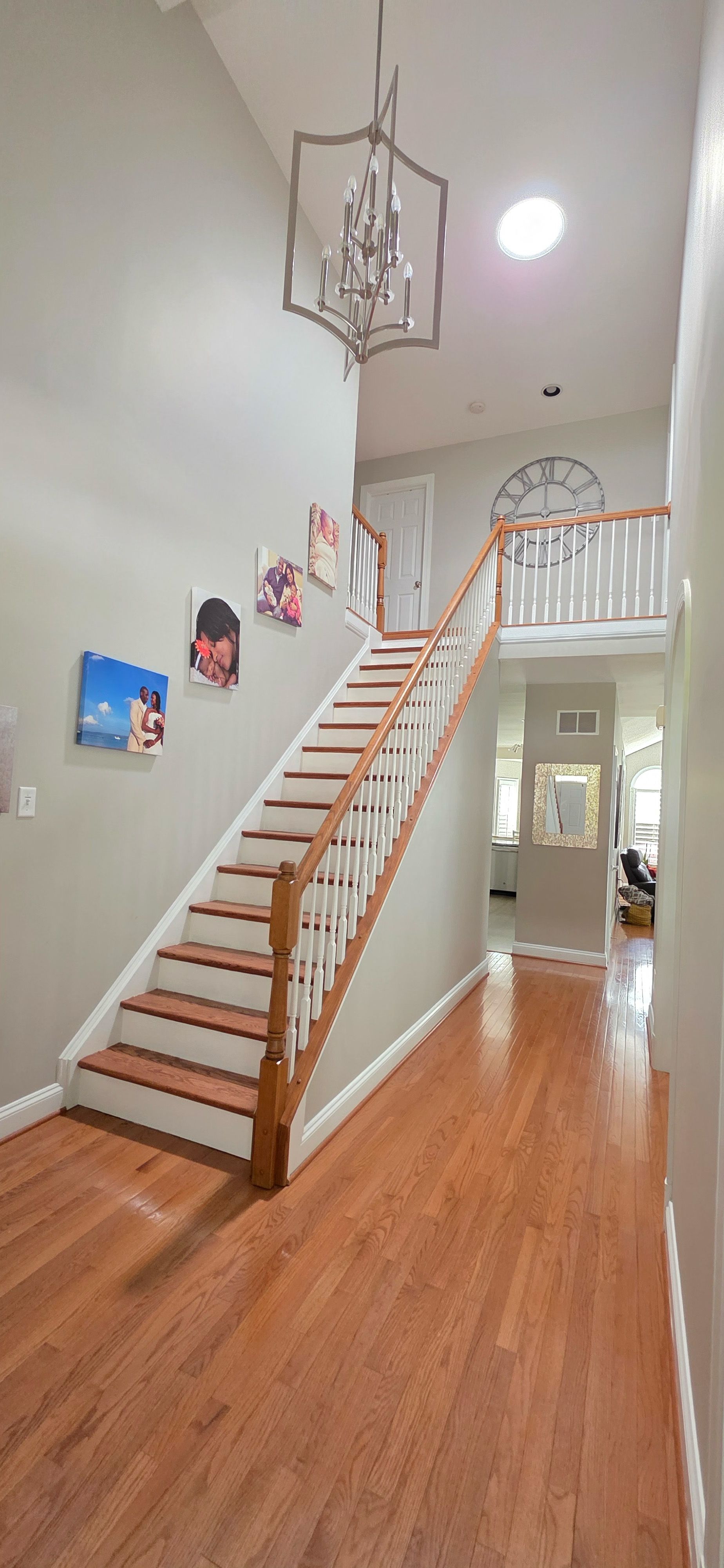 A light-filled foyer with wood flooring, a staircase with white railings, and a hanging geometric chandelier.