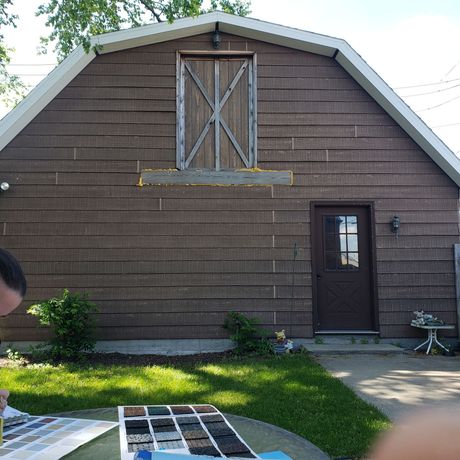 A man sits at a table in front of a barn