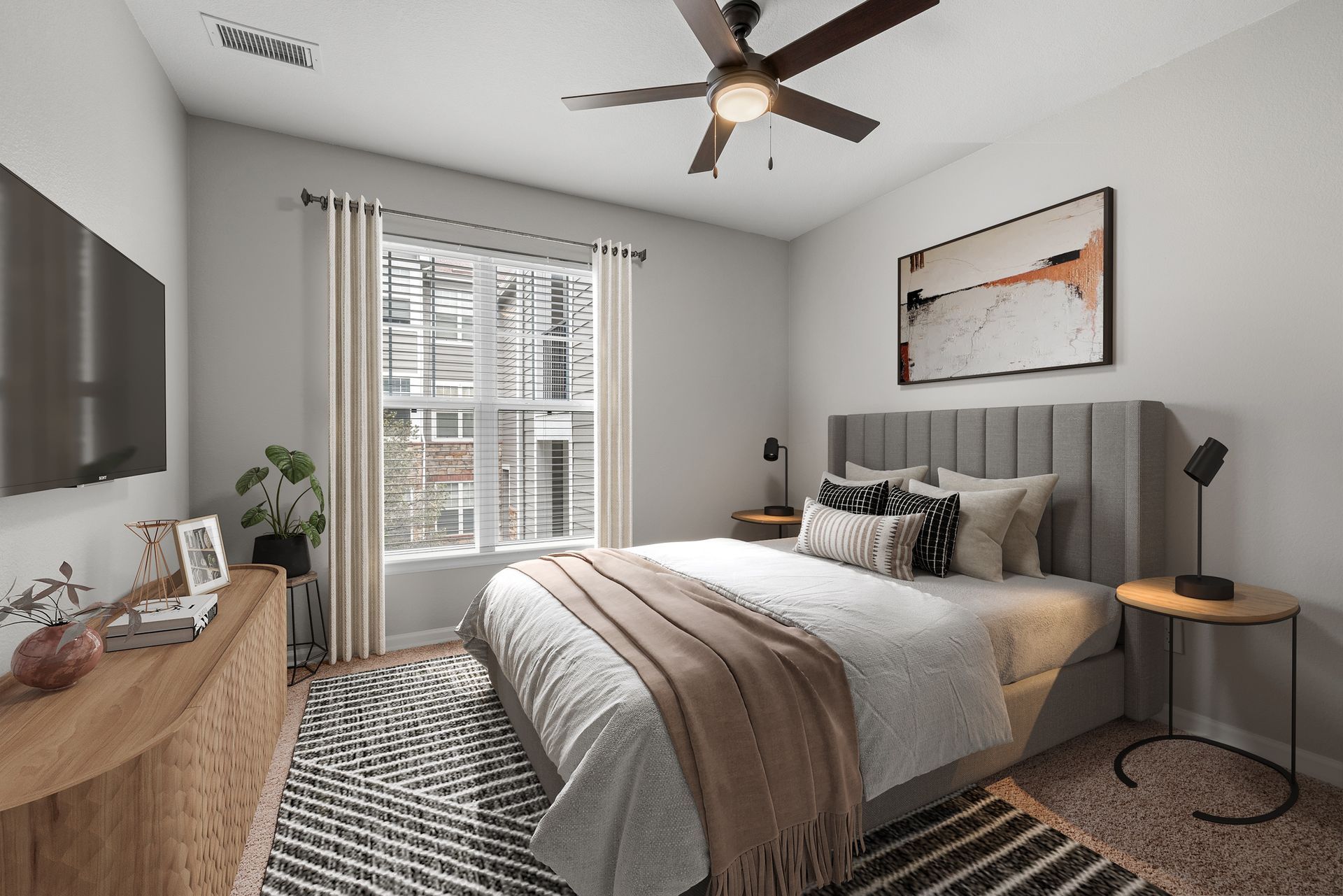Bedroom with gray upholstered bed, two round nightstands, ceiling fan, large window at Briargate on Main apartments in Parker, CO.