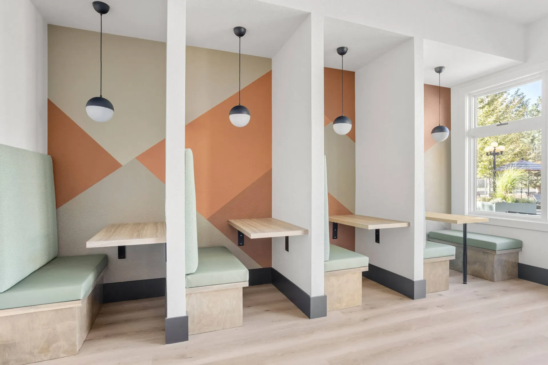 Interior community lounge with partitioned booth seating, pendant lights, and a geometric mural at Briargate on Main apartments in Parker, CO.