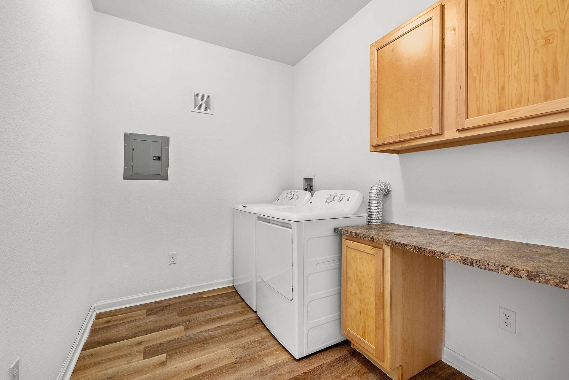 Laundry room with a top-load washer and dryer, wooden cabinets, and a laminate countertop at Briargate on Main apartments in Parker, CO.
