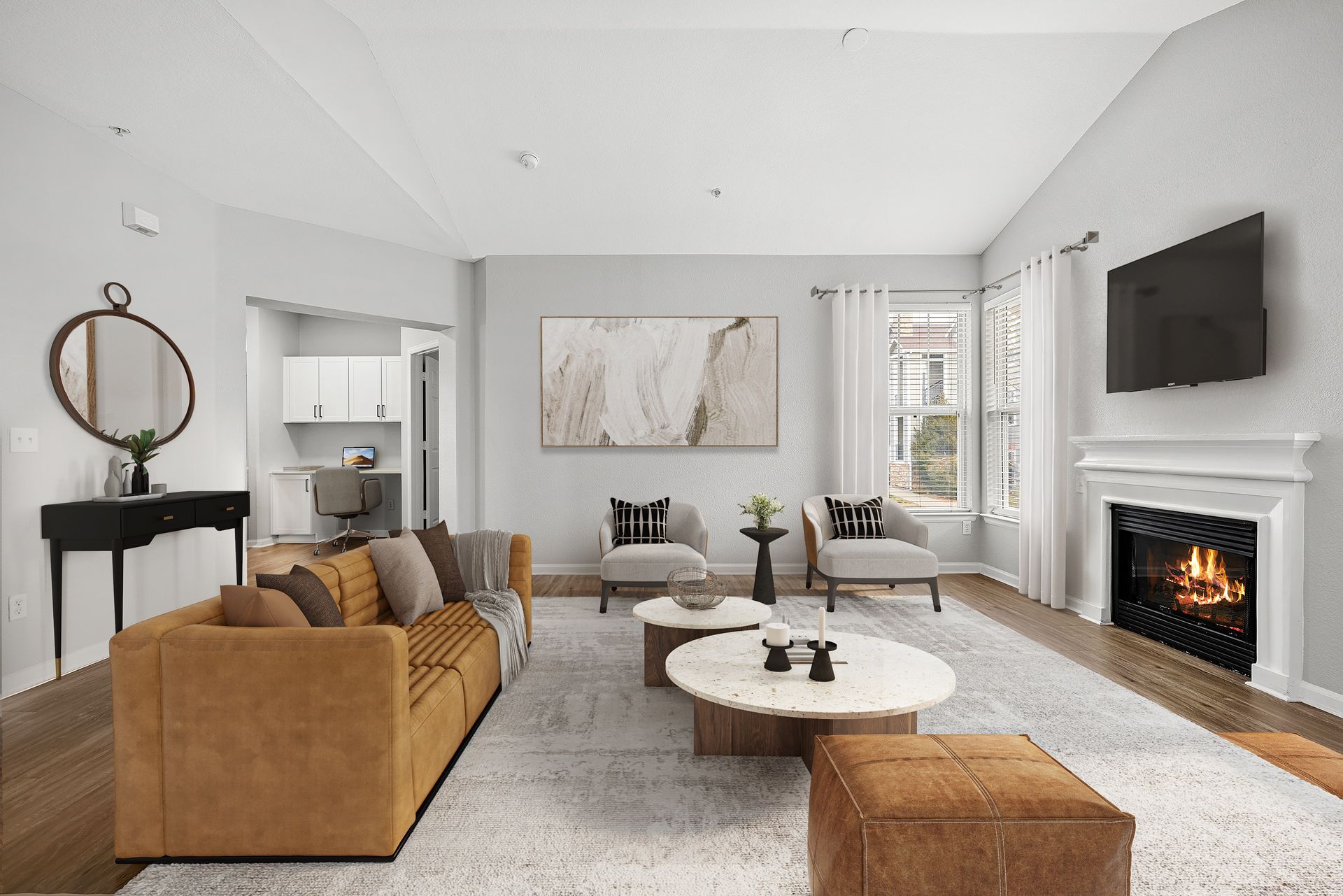 Spacious living room with a tan sofa, two gray armchairs, a fireplace, and a wall-mounted TV at Briargate on Main apartments in Parker, CO.